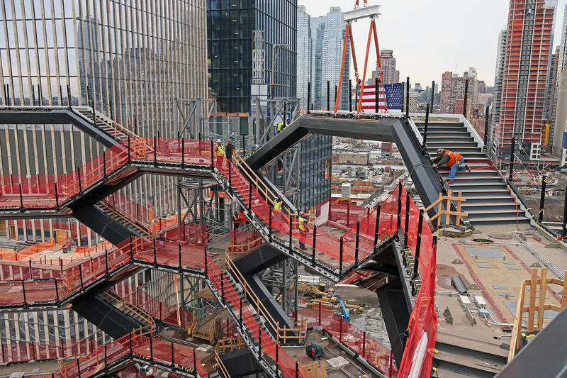 The topping out of <i>Vessel</i> shows several interconnecting stairwells with construction railings made of bright orange mesh material. The last landing being put into place is flying a large American flag.